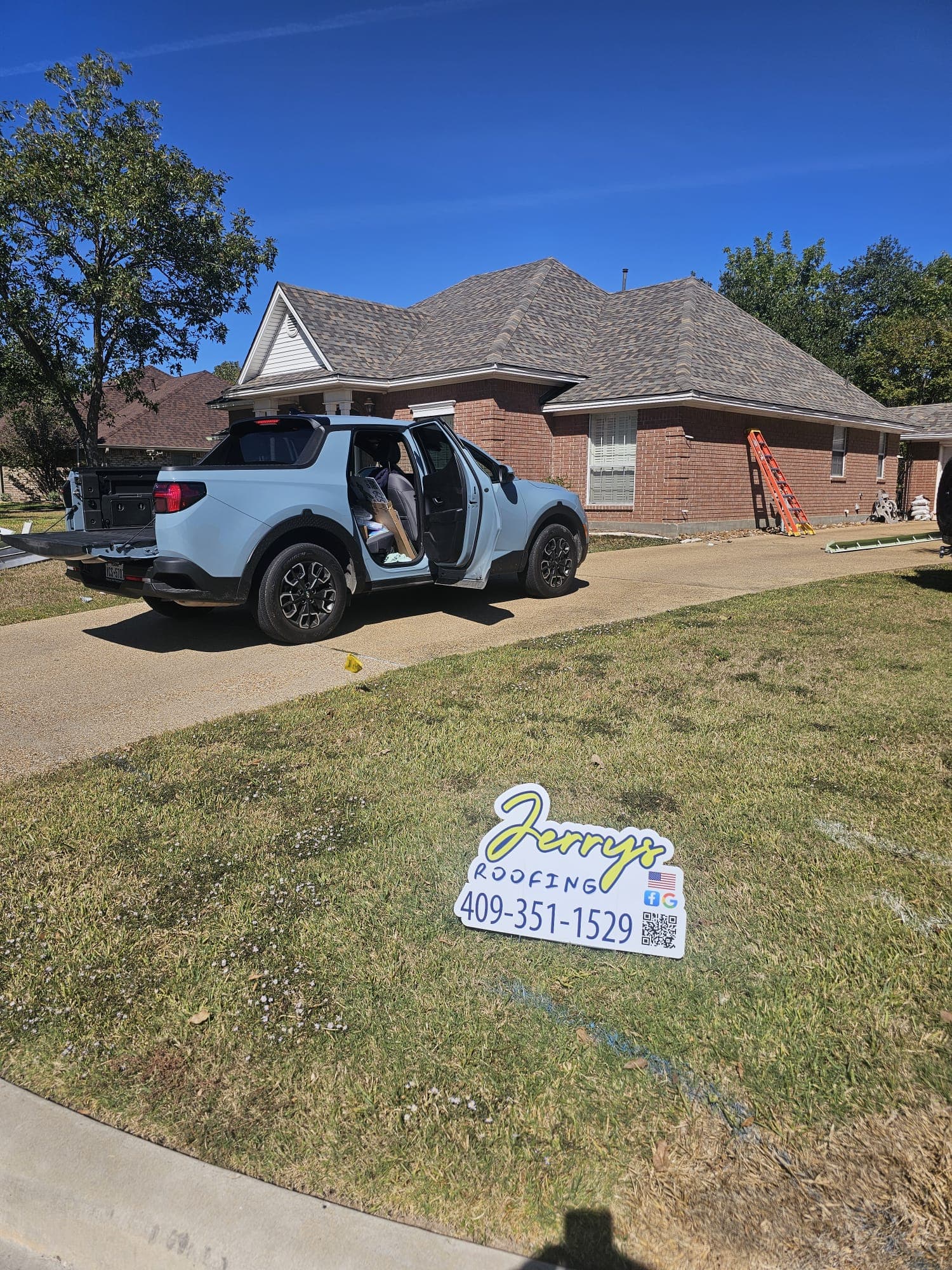 Jerrys Roofing light-blue Hyundai Santa Cruz truck with yard sign in front of an active job site in Katy, TX