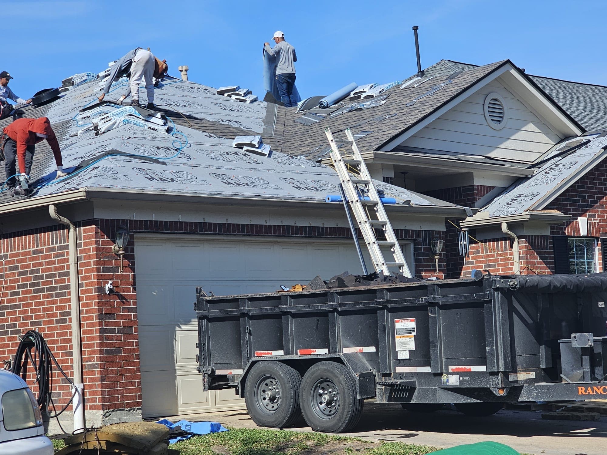Three Jerrys Roofing crew members actively tearing off and installing on a brick home in Katy