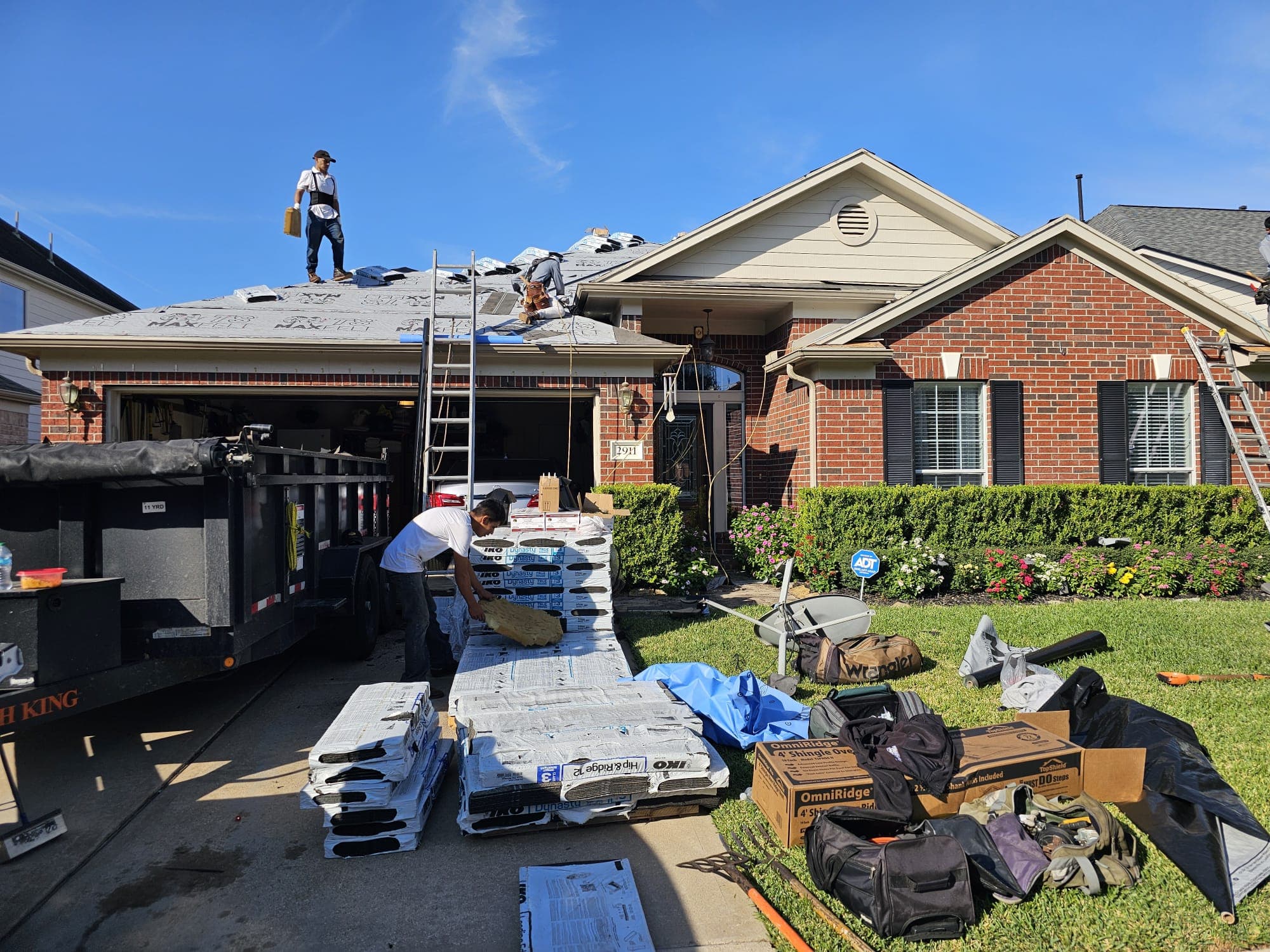 Pallets of architectural shingles staged in the driveway as crew works on the roof