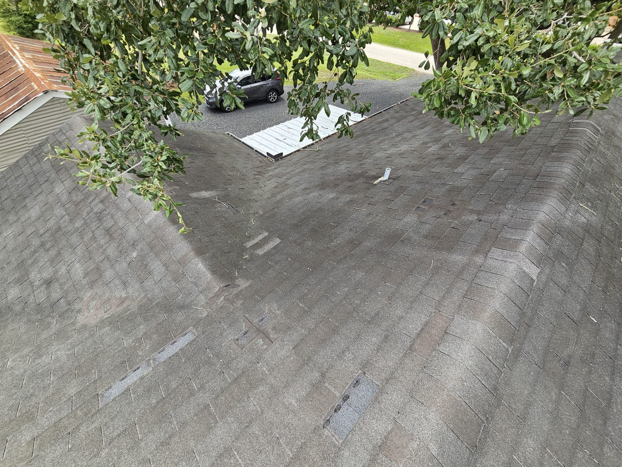 Inspection close-up of a worn roof valley with patched shingles and debris